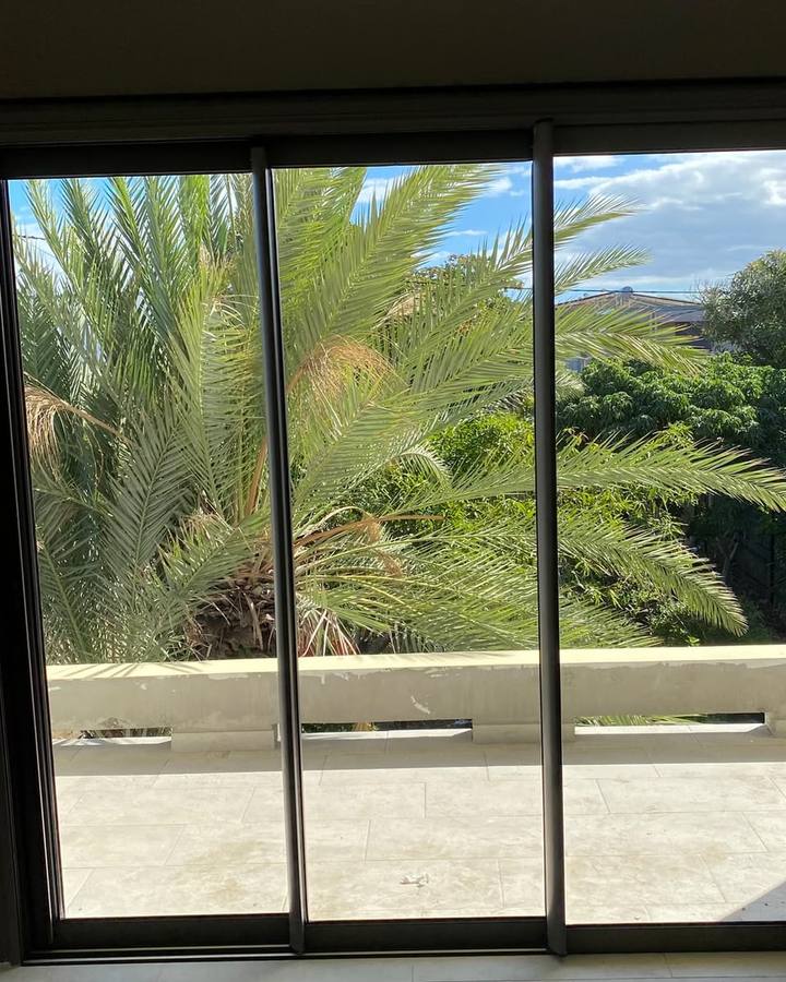 La même baie vitrée après nettoyage, vitrage clair sur le palmier et la terrasse