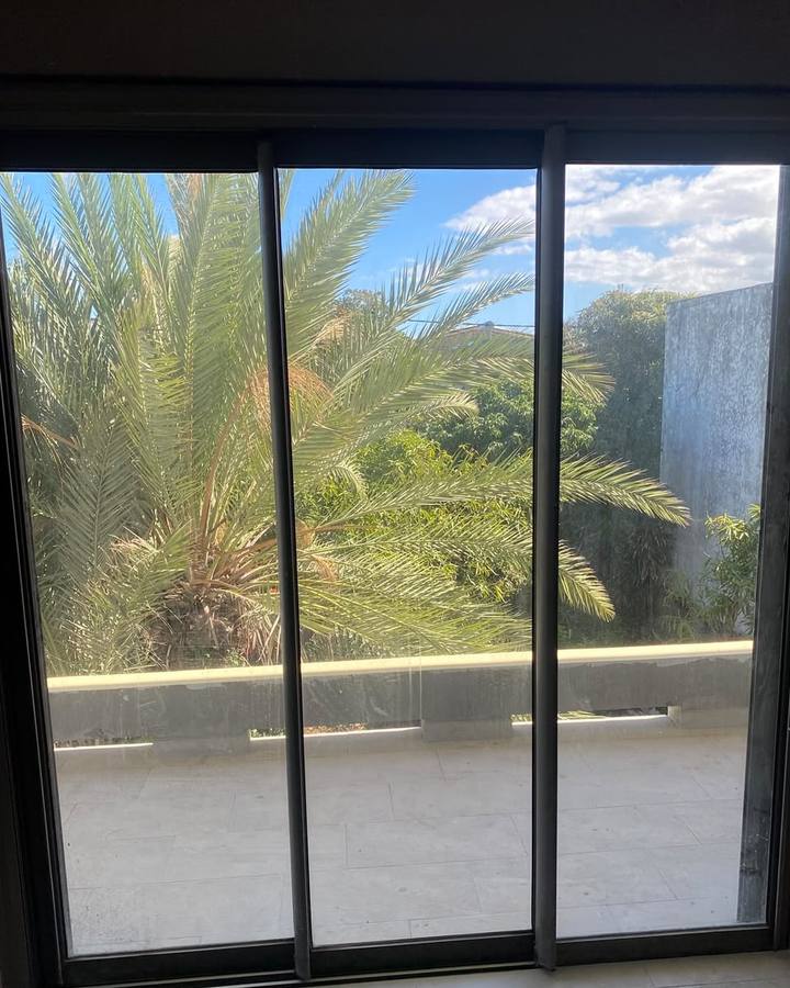 Baie vitrée coulissante à trois vantaux au vitrage terne, vue sur un palmier et une terrasse, avant nettoyage