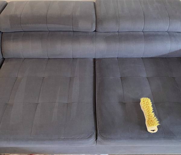 Brosse à main posée sur l’assise d’un canapé en tissu gris, zone brossée visible