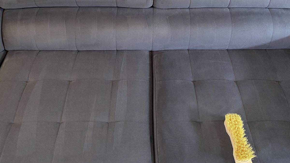 Brosse posée sur l’assise d’un canapé gris en tissu pendant un nettoyage