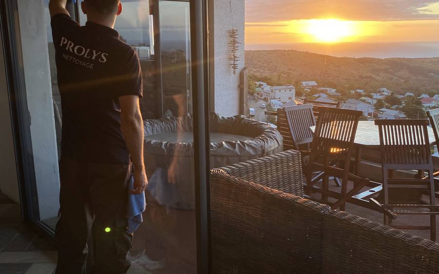 Intervenant Prolys nettoyant la baie vitrée d’un logement au coucher du soleil