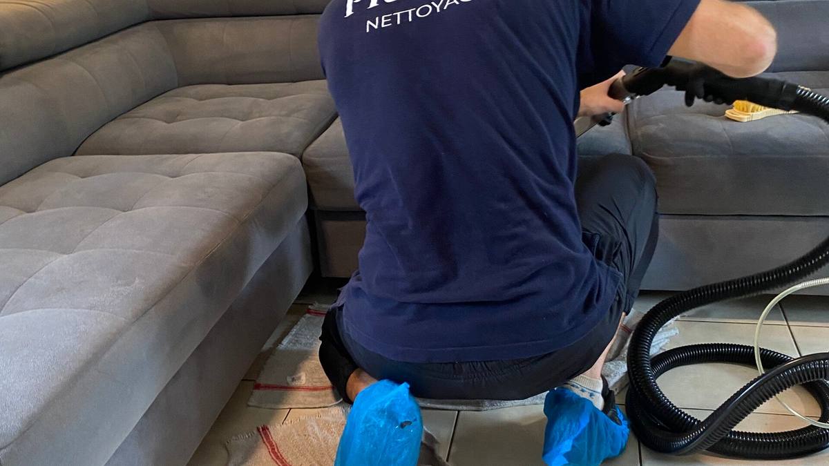 Intervenant Prolys, de dos, nettoyant en profondeur un canapé d’angle en tissu