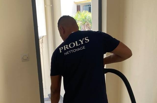 Intervenant Prolys, de dos, en tee-shirt Prolys Nettoyage, passant l’aspirateur près d’une porte-fenêtre