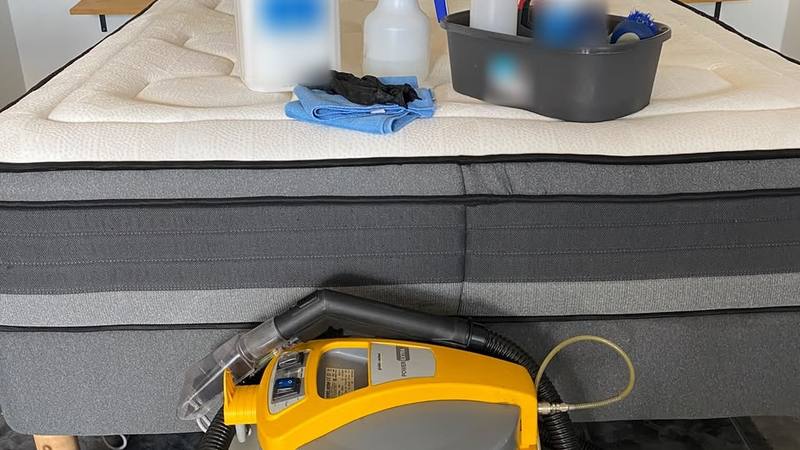 Machine de nettoyage professionnelle au pied d’un lit, pulvérisateurs et microfibres posés sur le matelas